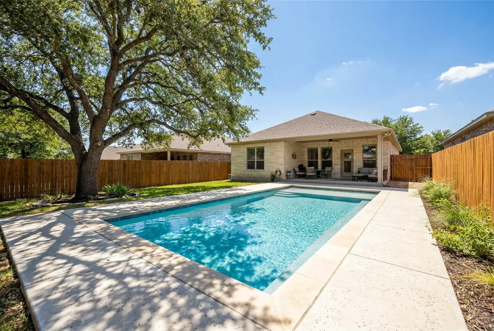 Backyard pool with a light concrete deck shaded by a live oak tree