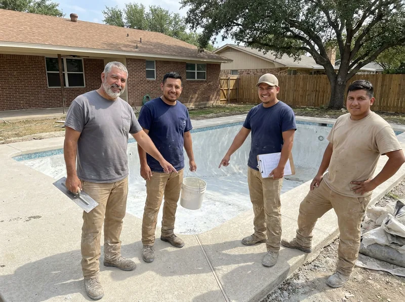 Four pool workers in plain work clothes beside a drained pool being replastered in a San Antonio backyard