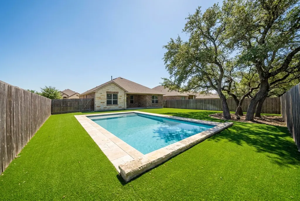 Artificial turf lawn around a rectangular backyard pool with live oak trees